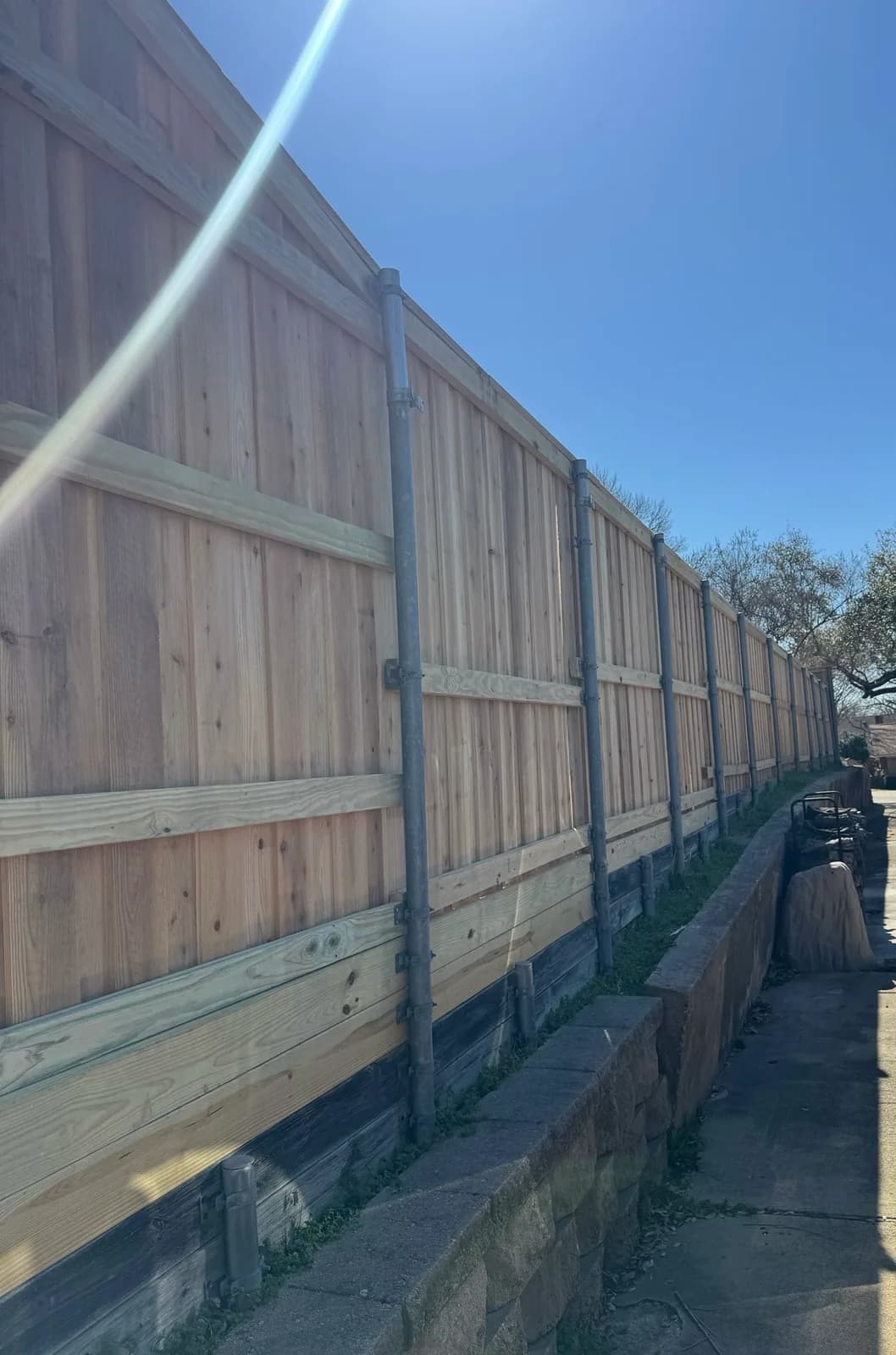 Cedar privacy fence on galvanized posts above a retaining wall.
