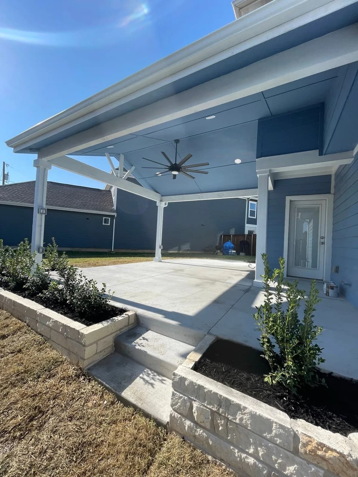 White patio cover with a ceiling fan over a poured patio.