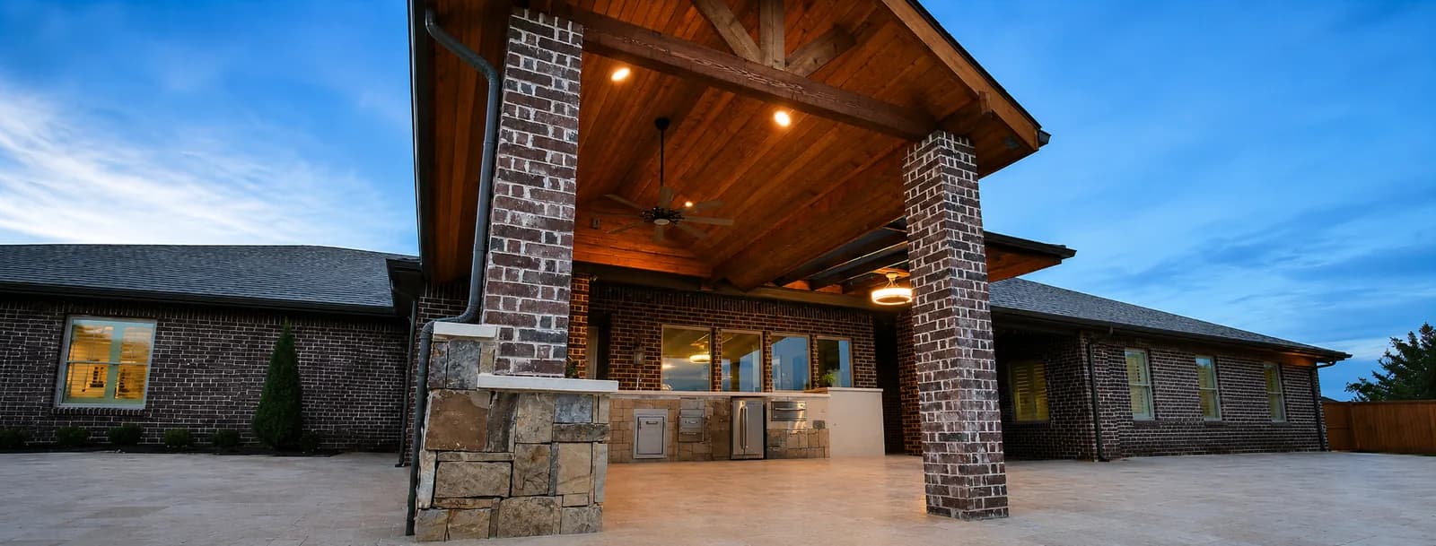 Brick-columned patio cover over an outdoor kitchen at dusk.
