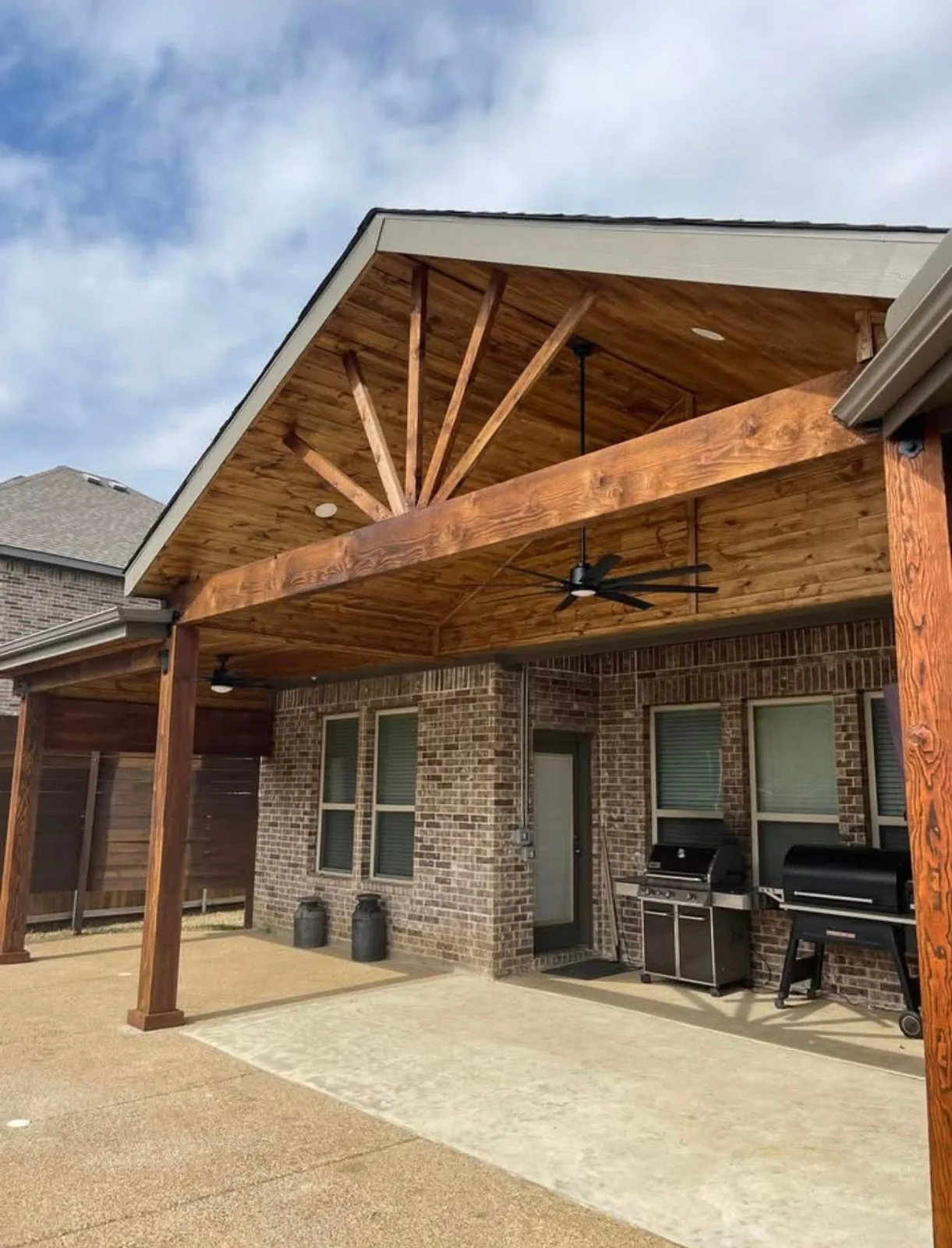 Gabled patio cover with exposed cedar rafters over a brick home.