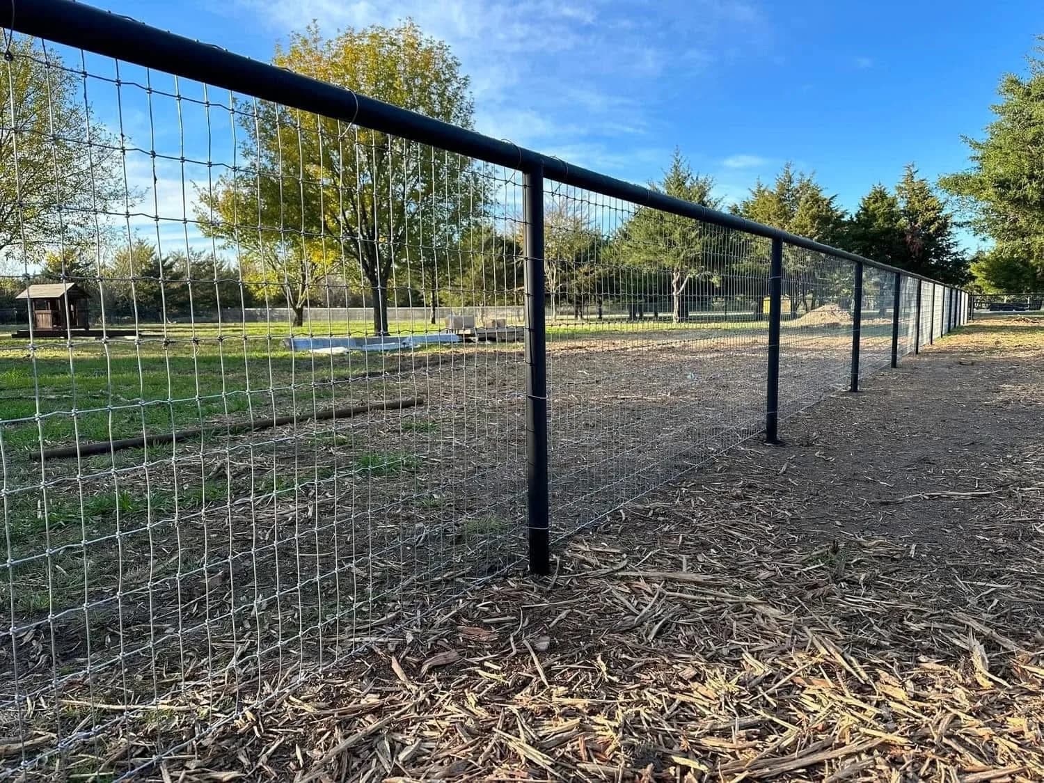 Black pipe top rail over woven wire fencing across open acreage.